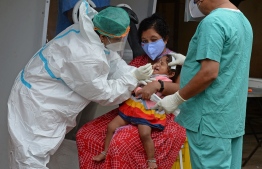 A health worker wearing personal protective equipment (PPE) gear collects a swab sample from a child at a free COVID-19 coronavirus testing centre in Hyderabad on August 19, 2020. - India's official coronavirus death soared past 50,000 on August 17 as the pandemic rages through smaller cities and rural areas where health care is feeble and stigmatisation rife. (Photo by NOAH SEELAM / AFP)