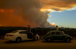 People watch the Walbridge fire, part of the larger LNU Lightning Complex fire, from a vineyard in Healdsburg, California on August 20, 2020. - A series of massive fires in northern and central California forced more evacuations as they quickly spread August 20, darkening the skies and dangerously affecting air quality. (Photo by JOSH EDELSON / AFP)