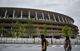 People walk past the newly-built Japan National Stadium, the main venue for the 2020 Olympic and Paralympic Games now postponed until July 2021 due to the COVID-19 coronavirus pandemic in Tokyo on August 23, 2020. (Photo by Charly TRIBALLEAU / AFP)