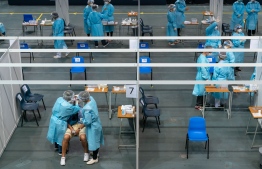 Medical workers collect samples from a man (bottom L, seated) at a makeshift testing site for COVID-19 coronavirus infections at the Queen Elizabeth Stadium in Hong Kong on September 1, 2020. - Hong Kong launched a mass coronavirus testing scheme on September 1, but calls for millions to take up the offer have been undermined by deep distrust of the government following China's crushing of the city's democracy movement. (Photo by Anthony Kwan / POOL / AFP)