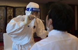 A worker in a protective suit takes a swab from a journalist to test for the Covid-19 coronavirus at a hotel in Beijing on September 7, 2020, a day ahead of a ceremony being held to honour people who were involved in the fight against the Covid-19 coronavirus. (Photo by NICOLAS ASFOURI / AFP)