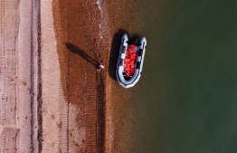 An aerial picture shows a man using a mobile telephone whilst standing next to a recently abandoned inflatable boat, used by migrants to cross the Straits of Dover from France to Deal on the south east coast of England, on September 14, 2020, after the migrants arrived on the beach. - Nearly 1,500 migrants and asylum-seekers arrived in Britain by small boats in August, according to an analysis by the domestic Press Association news agency. (Photo by BEN STANSALL / AFP)