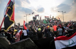(FILES) In this file photo taken on October 29, 2019, Iraqi protesters wave national flags as they stand atop concrete barriers across the capital Baghdad's al-Jumhuriya bridge which connects between Tahrir Square and the high-security Green Zone, hosting government offices and foreign embassies, during the ongoing anti-government protests. - In October 2019, unprecedented demonstrations across Iraq demanded the downfall of the ruling class. But after a year, a new government and nearly 600 protesters killed, virtually nothing has changed. PHOTO: AHMAD AL-RUBAYE / AFP