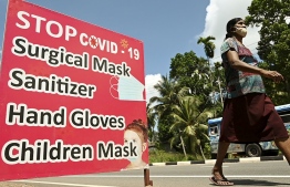 A woman wearing a facemask walks past a display featuring health and safety measures against the spread of the Covid-19 Coronavirus on a street in Piliyandala, a suburb of Sri Lanka's capital Colombo on October 23, 2020. (Photo by LAKRUWAN WANNIARACHCHI / AFP)