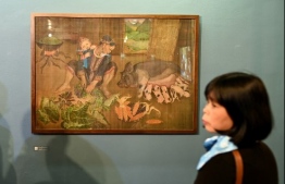 This photograph taken on October 22, 2020 shows a visitor looking at a painting by 89-year-old Vietnamese artist Mong Bich during the opening of her first solo exhibition at the French Cultural Centre in Hanoi. - Bich specialises in silk paintings of daily life and ordinary people, women in particular, and ploughed a lonely furrow during many years of war when artists were steered towards the army or frontline workers as subjects. (Photo by Manan VATSYAYANA / AFP) /