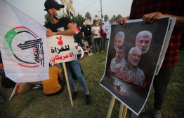 A man stands with a sign reading in Arabic "no to American invaders" as another stands with a sign showing the faces of slain (top L-R) Iranian commander Qassem Soleimani, and Iraqi paramilitary commander Abu Mahdi Al-Muhandis, and (bottom L) Abu Montazer al-Muhammadawi during a demonstration outside the entrance to the Iraqi capital Baghdad's highly-fortified Green Zone on November 7, 2020, demanding the departure of remaining US forces from Iraq. - Several hundred protesters gathered in the Iraqi capital on Saturday afternoon to demand US troops leave the country in accordance with a parliament vote earlier this year. (Photo by AHMAD AL-RUBAYE / AFP)