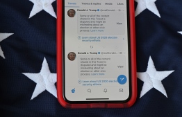 This illustration photo shows a mobile phone placed on a US flag with Tweets from US President Donald Trump masked with warnings imposed by Twitter stating that they may be incorrect. (Photo by Robyn Beck / AFP)
