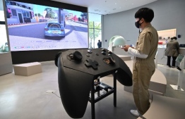 A staff member plays a game in front of an oversized mock-up of Microsoft's Xbox controller at a flagship store of SK Telecom in Seoul on November 10, 2020. (Photo by Jung Yeon-je / AFP)