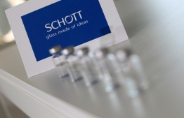 Pharmaceutical vials made by German glass company Schott are pictured next to the Schott logo at the company's headquarters in Mainz, western Germany, on November 20, 2020. - As expectations grow that the first Covid-19 jabs will be administered in a matter of weeks, German glassmaker Schott is quietly doing what it has been for months: churning out vials that will hold the vaccine. (Photo by Daniel ROLAND / AFP)