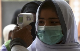 A school official checks the body temperature of students wearing facemasks as they enter a school amid the Covid-19 coronavirus pandemic in Karachi on November 25, 2020. (Photo by Asif HASSAN / AFP)