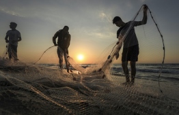 Palestinian fishermen gather their net along a beach in Gaza City at sunset on December 2, 2020. (Photo by MAHMUD HAMS / AFP)
