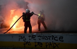 Firefighters try to extinguish the fire from a car near a graffiti reading "No justice, no peace" during a demonstration for 'social rights' and against the 'global security' draft law, which Article 24 would criminalise the publication of images of on-duty police officers with the intent of harming their 'physical or psychological integrity', in Paris, on December 5, 2020. (Photo by Anne-Christine POUJOULAT / AFP)