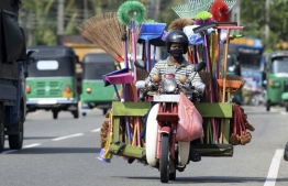 A street vendor selling housewares drives his motorcycle along a road in Colombo December 15, 2020. (Photo by LAKRUWAN WANNIARACHCHI / AFP)