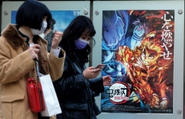 In this picture taken on December 16, 2020, pedestrians walk past a poster promoting the anime movie Demon Slayer -- Kimetsu no Yaiba the Movie: Mugen Train -- at a cinema in Tokyo. - An anime epic in which a teenager hunts down and beheads demons has become the surprise sensation of Japanese cinema during the pandemic, and could soon be the country's top-grossing film of all time. (Photo by Kazuhiro NOGI / AFP) / To go with AFP story  Japan-entertainment-film-anime-health-virus, FOCUS by Mathias CENA, Katie Forster