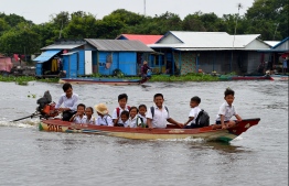 This photo taken on October 14, 2020 shows students sitting in a boat travelling from school in Prek Toal floating village in Battambang province. - More than a million people live on or around Tonle Sap lake, the world's largest inland fishery, but as a result of climate change and dams upstream on the Mekong, water levels are falling and fish stocks are dwindling. (Photo by TANG CHHIN Sothy / AFP) /