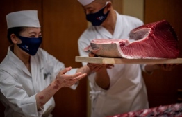 Chef Akifumi Sakagami (R) passes a piece of meat from one of the auctioned tuna to a staff member at a restaurant in Ginza, after the New Year's auction at Toyosu fish market in Tokyo on January 5, 2021. (Photo by Philip FONG / AFP)
