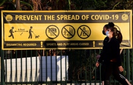 Pedestrians wearing facemasks walk past a prevent the spread of Covid-19 banner in Los Angeles, California on January 19, 2020. (Photo by Frederic J. BROWN / AFP)