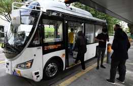 An employee (2nd R) checks the commuter application booking on a passenger's mobile phone before boarding an on-demand autonomous bus developed by ST Engineering at the start of a trial run from Singapore Science Park 2 to Haw Par Villa MRT station in Singapore on January 26, 2021. (Photo by Roslan RAHMAN / AFP)