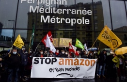 Demonstrators hold a banner reading "Stop Amazon and its world" and wave flags as they gather to protest against Amazon implantation, in front of the Perpignan Mediterranee Metropole headquarters in Perpignan, on January 30, 2021. (Photo by RAYMOND ROIG / AFP)