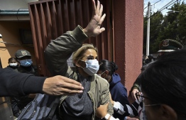 Former Bolivian president Jeanine Anez waves as she is escorted by members of the Special Force Against Crime (FELCC) into the Obrajes prison in La Paz on March 15, 2021, after a judge ordered four months of preventive custody. - Anez was arrested on March 13 on terrorism and sedition charges over what the government claims was a coup attempt against her predecessor and political rival Evo Morales. (Photo by Aizar RALDES / AFP)