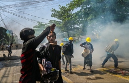 A protesters pours Coca-Cola on the face of a comrade to diminish the effects of tear gas during a crackdown by security forces on a demonstration against the military coup in Yangon's Thaketa township on March 19, 2021. (Photo by STR / AFP)