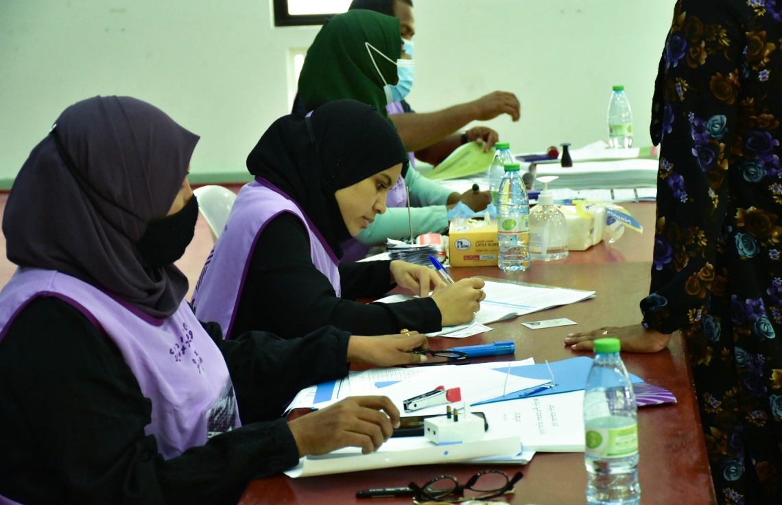 ބ. އޭދަފުށި: އޭޕްރިލް 10، 2021: ލޯކަލް ކައުންސިލް އިންތިހާބުގައި އޭދަފުށި ވޯޓުލާ މަރުކަޒުގައި މީހަކު ވޯޓުލުމަށް އޮފިޝަލުންގެ މޭޒުކައިރީގައި މައުލޫމާތު ޗެކް ކުރަނީ.-- ފޮޓޯ: ނިޔަމި