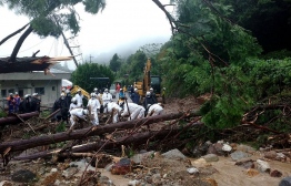 This handout picture taken and released by Nagasaki Kenou Fire Department on August 14, 2021 shows rescue workers searching for missing persons at the site of a mudslide caused by heavy rain in Unzen, Nagasaki Prefecture -- Photo by Handout / Nagasaki Kenou Fire Department / AFP