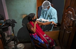 An army health official (R) inoculates a woman with a dose of the Covid-19 coronavirus during a mobile vaccination drive in Colombo on August 12, 2021. (Photo by Ishara S. KODIKARA / AFP)