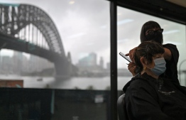 A woman gets her hair cut at a salon near the Sydney Harbour Bridge on October 11, 2021, as Sydney ended their lockdown against the Covid-19 coronavirus after 106 days. -- Photo: Steven Saphore / AFP
