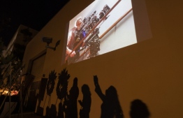 A photo of cinematographer Halyna Hutchins is seen above the shadows of people approaching a memorial table during a candlelight vigil for Hutchins, who was accidentally killed by a prop gun fired by actor Alec Baldwin, in Burbank, California on October 24, 2021. -- Photo: David McNew/ AFP