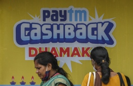 In this picture taken on November 7, 2021 women sit next to a billboard advertisement for Paytm, an Indian cellphone-based digital payments platform, in Mumbai. -- Photo: Punit Paranjpe / AFP