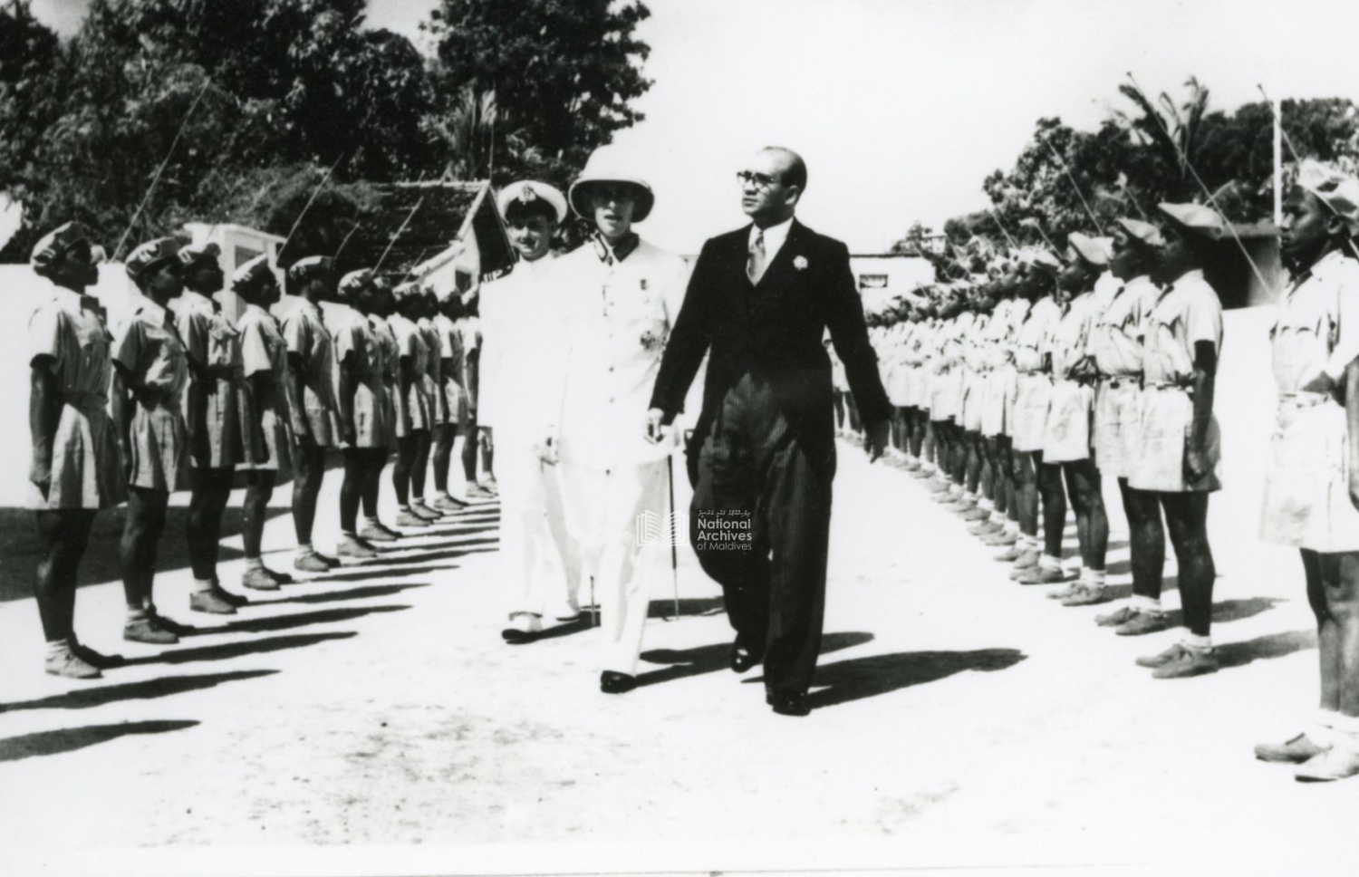 ޖުމްހޫރީ ދުވަހު ރައީސް މުހައްމަދު އަމީން މުލީއާގެއަށް ވަޑައިގަންނަވަނީ. އަމީންގެ ފަހަތްޕުޅުގައި އެ ހުންނެވީ އިނގިރޭސި ހައި ކޮމިޝަނަރު ހެންކިންސަން. -- ފޮޓޯ: ނެޝަނަލް އާކައިވް