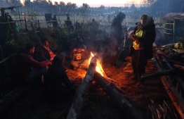 A picture taken on November 10, 2021 shows migrants warming themselves by a bonfire in a camp on the Belarusian-Polish border in the Grodno region. - Hundreds of desperate migrants are trapped in freezing temperatures on the border and the presence of troops from both sides has raised fears of a confrontation. -- Photo: Ramil Naibulin/ BELTA / AFP
