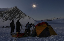 This handout picture released by Imagen Chile shows Chilean and US scientists looking at a solar eclipse from the Union Glacier in Antarctica on December 4, 2021. -- Photo: Felipe Trueba / Imagen Chile / AFP
