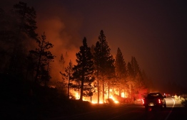 (FILE) A truck passes a spot fire from the Caldor Fire burning along Highway 89 near South Lake Tahoe, Calif., on Sept. 2. -- Photo: Jae C. Hong / AP