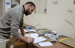 A worker at the Mosul Museum takes notes while analysing artefact fragments to be reconstructed and reassembled at the Mosul Museum in Iraq's northern city on December 14, 2021. - In the damaged Mosul Museum, Iraqis supported by French restoration workers sort through the fragments of 2,500-year-old remains destroyed by jihadists, part of efforts aiming for reconstruction. -- Photo: Zaid Al-Obeidi/ AFP