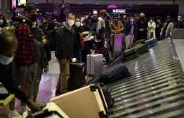 Airline passengers wearing face masks wait to collect bags from a baggage carousel at the Harry Reid International Airport (LAS) on January 2, 2022 in Las Vegas, California. - Americans returning home from holiday travel had to battle another day of airport chaos on January 2, with more than 2,000 flights cancelled due to bad weather or airline staffing woes sparked by a surge in Covid cases. -- Photo: Patrick T. Fallon / AFP