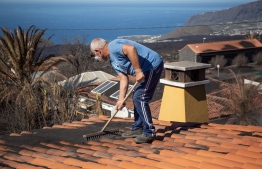 61 year-old mason Felix Rodriguez Luis removes ashes from the roof of his house, situated in an exclusion zone due to the volcanic risk, following the Cumbre Vieja volcano's eruption, in the Las Manchas neighborhood on the Spanish Canary Island of La Palma on January 4, 2022. -- Photo: Desiree Martin / AFP