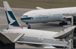(FILES) This file photo taken on March 15, 2017 shows a Cathay Pacific Boeing 777 passenger aircraft (top) taxiing past a stationary plane on the tarmac at the international airport in Hong Kong. - Cathay Pacific is being investigated and faces possible legal action over an Omicron variant coronavirus outbreak in Hong Kong that began with the airline's employees, the city's leader said on January 11, 2022. -- Photo: Anthony Wallace / AFP