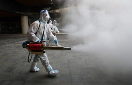 (FILE) Staff members wearing personal protective equipment (PPE) spray disinfectant outside a shopping mall in Xi'an in north China's Shaanxi province on January 11, 2022. -- Photo: AFP