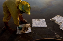 A worker cleans up crude oil on Mae Ram Phueng beach following a spill caused by a leak in an undersea pipeline owned by Star Petroleum Refining Public Company Limited (SPRC) in Rayong on January 29, 2022. -- Photo: Jack Taylor/ AFP