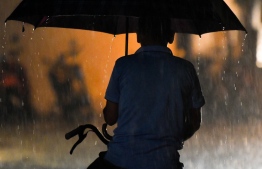 A local riding a bicycle with an umbrella during a previous stream of rainfall in the city of Male'.