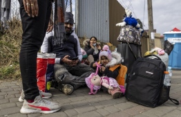 Family from India rest on the pavment as refugees from many different countries - from Africa, Middle East and India - mostly students of Ukrainian universities are seen at the Medyka pedestrian border crossing fleeing the conflict in Ukraine, in eastern Poland on February 27, 2022. - As Ukraine braces for a feared Russian invasion, its EU member neighbours are making preparations for a possible influx of hundreds of thousands or even millions of refugees fleeing military action. (Photo by Wojtek RADWANSKI / AFP)