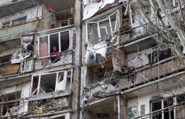A resident uses a dustpan and broom (top) to clear the debris from a flat, as another looks out of the destroyed front of a room, in a multi-storey building that was badly damaged as a result of Russian missile explosion after it was shot down over the city by Ukrainian air defence on March 6, in Kramatorsk on March 7, 2022. -- Photo: Anatolii Stepanov / AFP