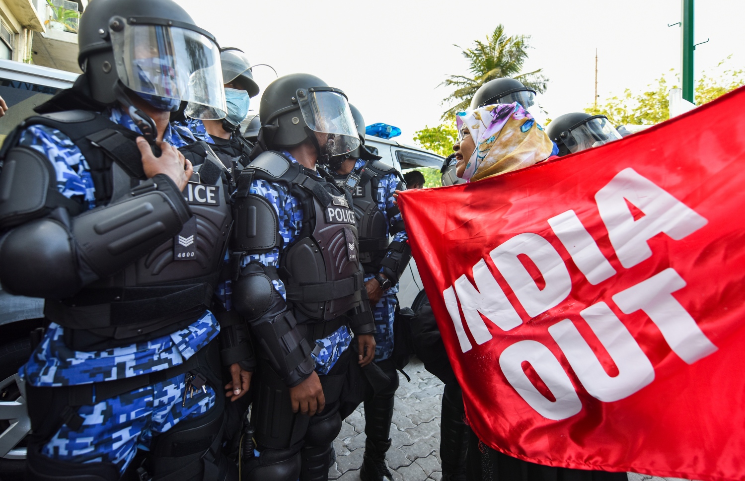 މުޒާހަރާގެ ބައިވެރިއަކު "އިންޑިއާ އައުޓް" ލިޔެފައި ވާ ފޮތިގަނޑެއްހިފައިގެން ފުލުހުންގެ ސަފުތައްކައިރީ މުޒާހަރާކުރަނީ -- ފޮޓޯ: ފަޔާޒު މޫސާ / މިހާރު