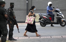 A pedestrian walks past soldiers standing on guard along a street in Colombo on April 2, 2022. - Troops armed with sweeping powers to detain suspects were deployed in Sri Lanka, hours after the president declared a state of emergency as protests against him escalated. (Photo by Ishara S. KODIKARA / AFP)
