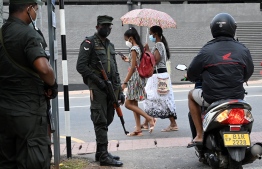 Pedestrians walk past soldiers standing on guard along a street in Colombo on April 2, 2022. - Troops armed with sweeping powers to detain suspects were deployed in Sri Lanka, hours after the president declared a state of emergency as protests against him escalated. (Photo by Ishara S. KODIKARA / AFP)