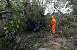 A municipal worker uses a chainsaw to cut branches on a tree that fell on a car in Pinetown, near Durban, on April 12, 2022. At least five people have been killed in floods and mudslides across South Africa's port city of Durban following heavy rains in recent days. Days of rains have flooded several areas and shut dozens of roads across the city --Photo: Phill Magakoe / AFP)