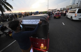A protester applies a sticker on a passing auto rickshaw during an ongoing anti-government demonstration near the president's office in Colombo on April 17, 2022, demanding the resignation of President Gotabaya Rajapaksa over the country's crippling economic crisis. -- Photo: Ishara S. Kodikara / AFP