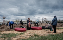 Nadia (R) attends the funeral of her husband and two other victims killed, conducted by Andrii Holovine (C), priest of the church of St. Andrew Pervozvannoho All Saints, at a cemetery in Bucha, on April 18, 2022, during the Russian invasion of Ukraine. -- Photo: Yasuyoshi Chiba / AFP